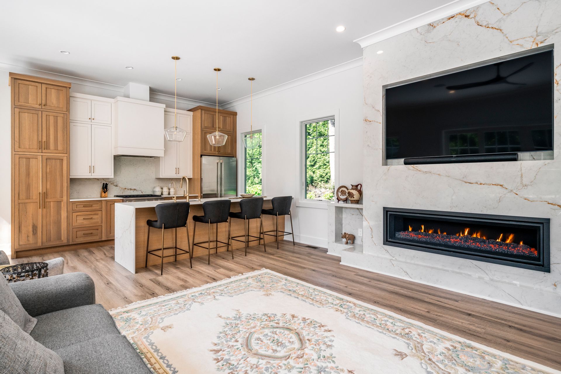 Modern open-concept living space with kitchen island and fireplace, featuring hardwood floors and a decorative rug.