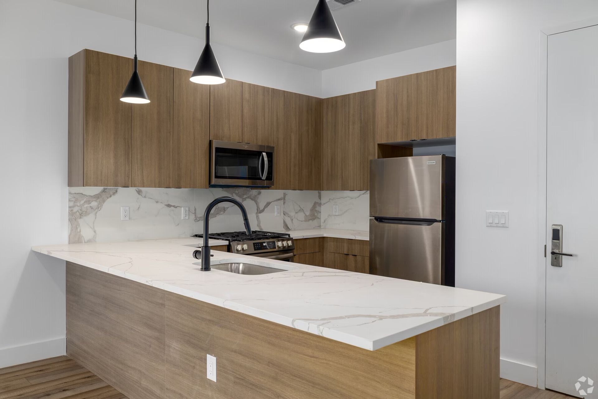 Modern kitchen with wood cabinets, white countertops, stainless steel appliances, and black pendant lights.