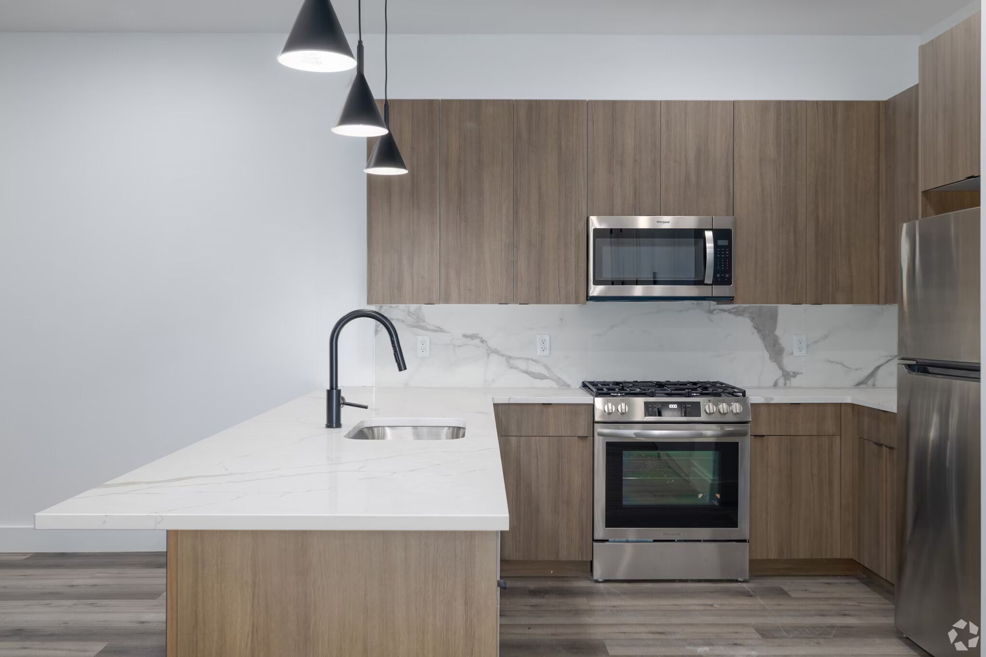 Modern kitchen with light wood cabinets, white countertops, and stainless steel appliances.