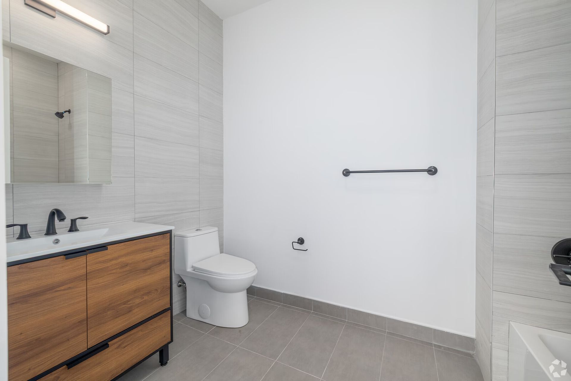 Modern bathroom with wood vanity, white toilet, and gray tiled walls and floor.
