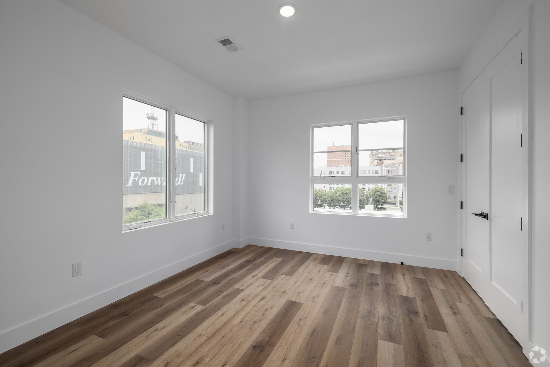 Empty room with wooden floor, white walls, and three windows.