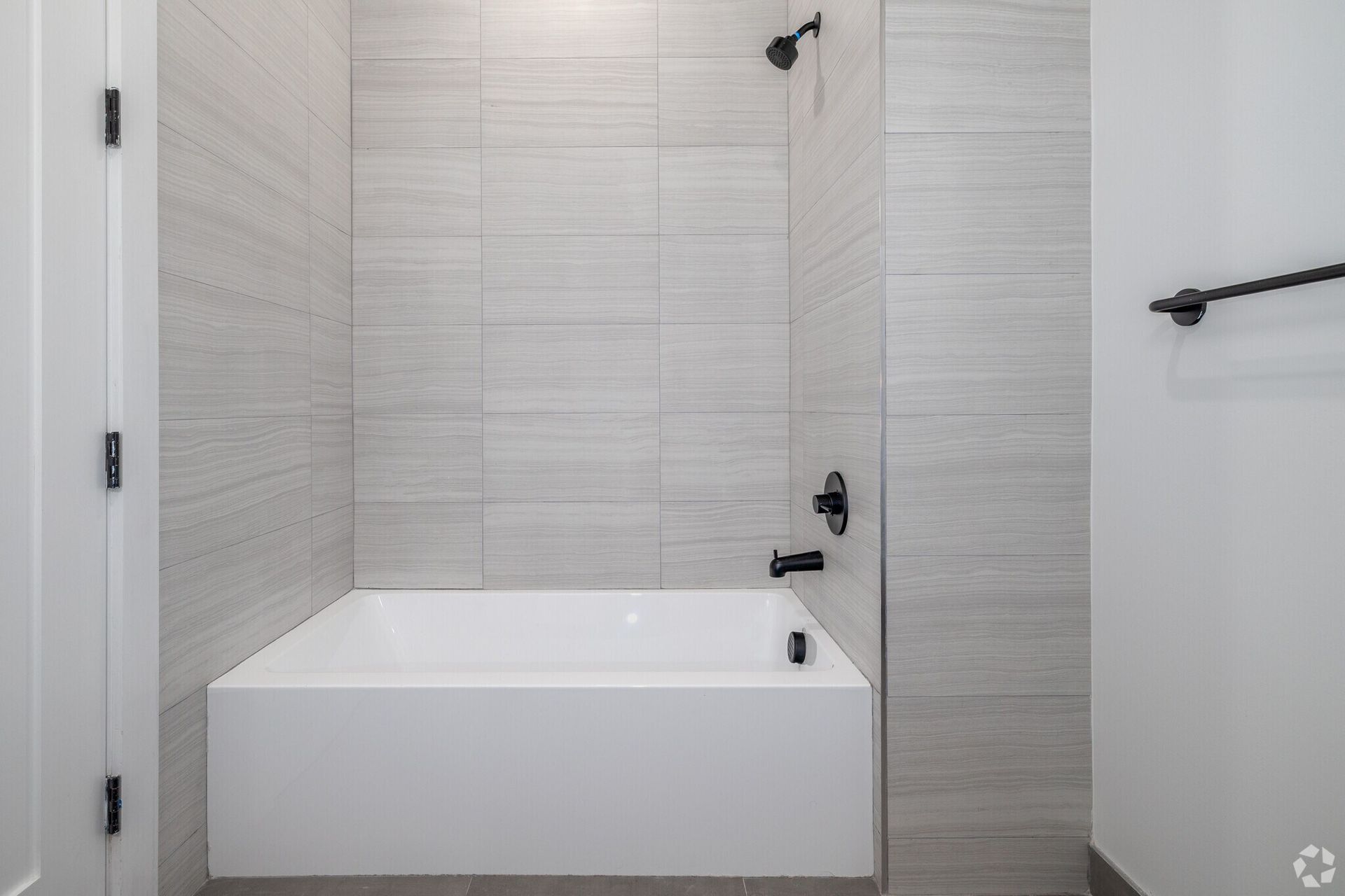White bathtub in a modern bathroom with gray tile walls and black fixtures.