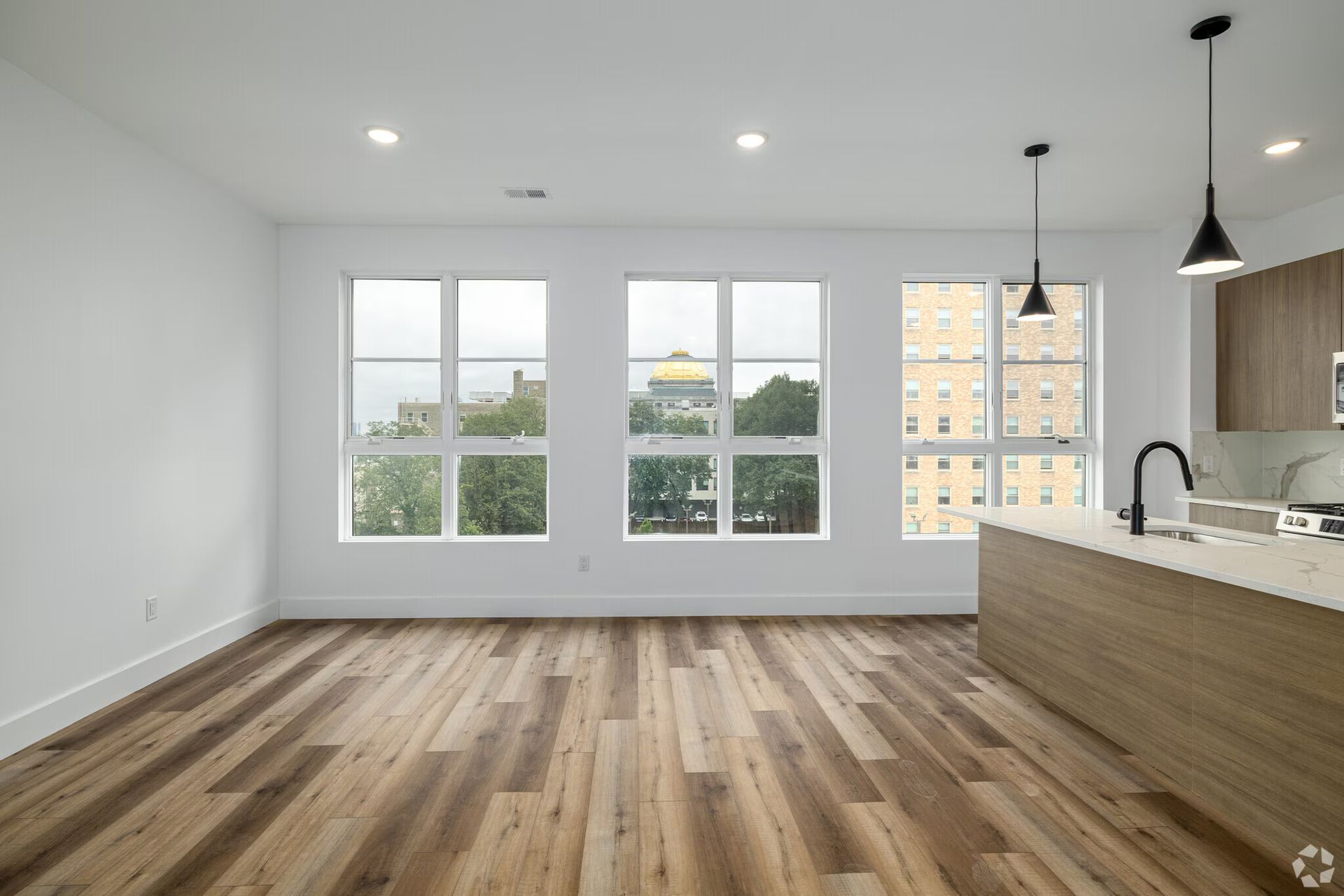 Empty modern apartment interior with wood flooring, large windows, and kitchen island.