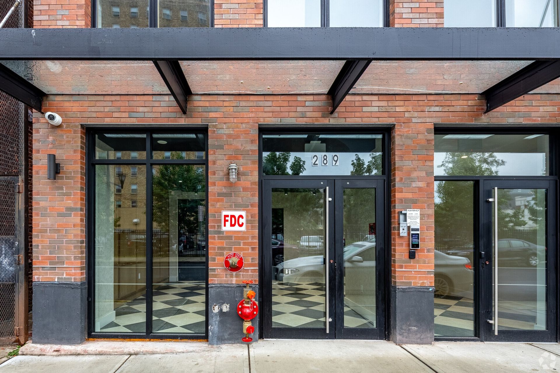 Exterior of a brick building with glass doors and a black awning. FDC sign and red fire hydrant visible.