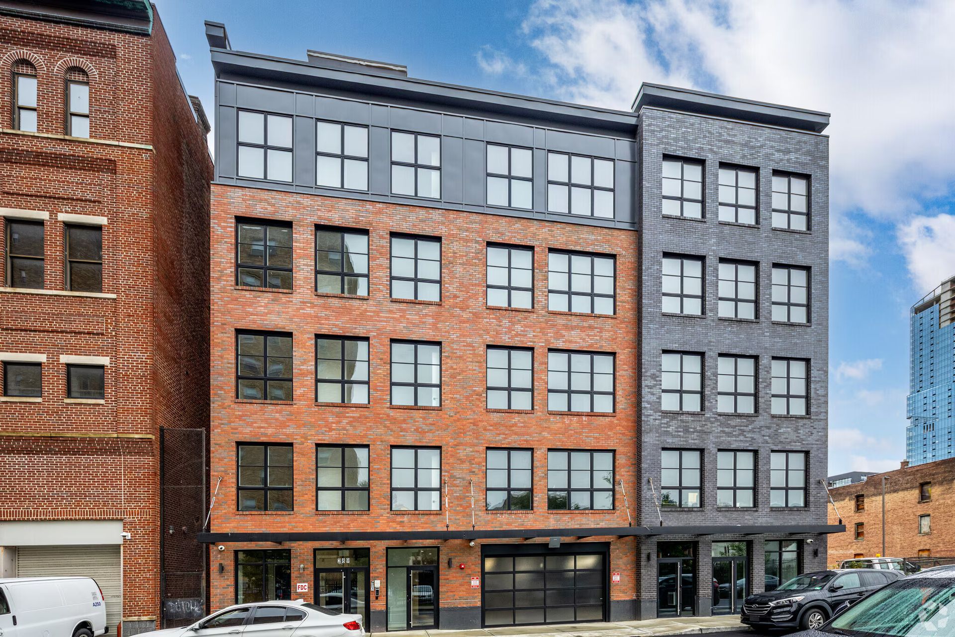 Multi-story brick and grey buildings with large windows, parked cars on street.