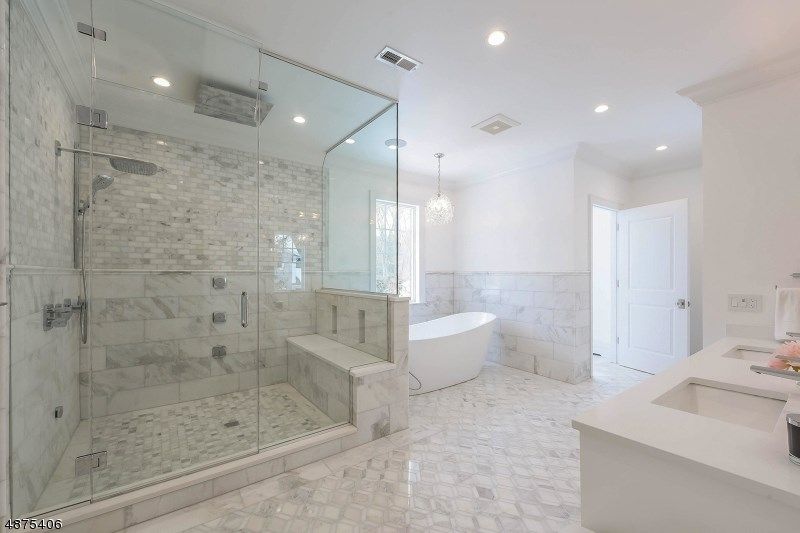 Spacious white bathroom with a glass-enclosed shower, freestanding tub, marble tiling, and double vanity.