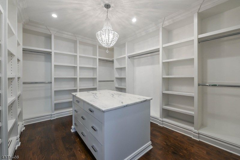 Walk-in closet with white shelves and drawers, dark wood floor, marble-topped island, and a chandelier.