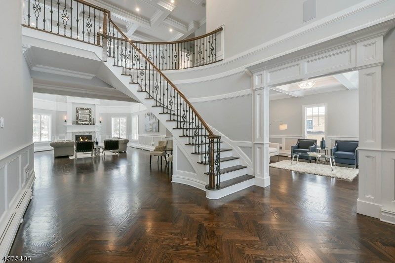 Elegant foyer with curving staircase, dark wood floors, white walls, and ornate railings.