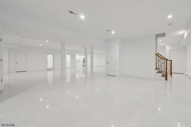 Empty, bright white basement with polished floor, support columns, and stairs with wooden railing.