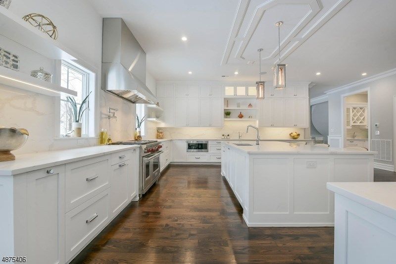 White modern kitchen with stainless steel appliances, dark wood floors, and island.