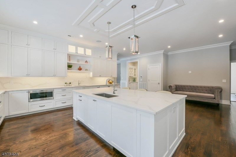Bright white kitchen with a large island, marble countertops, and dark wood floors.