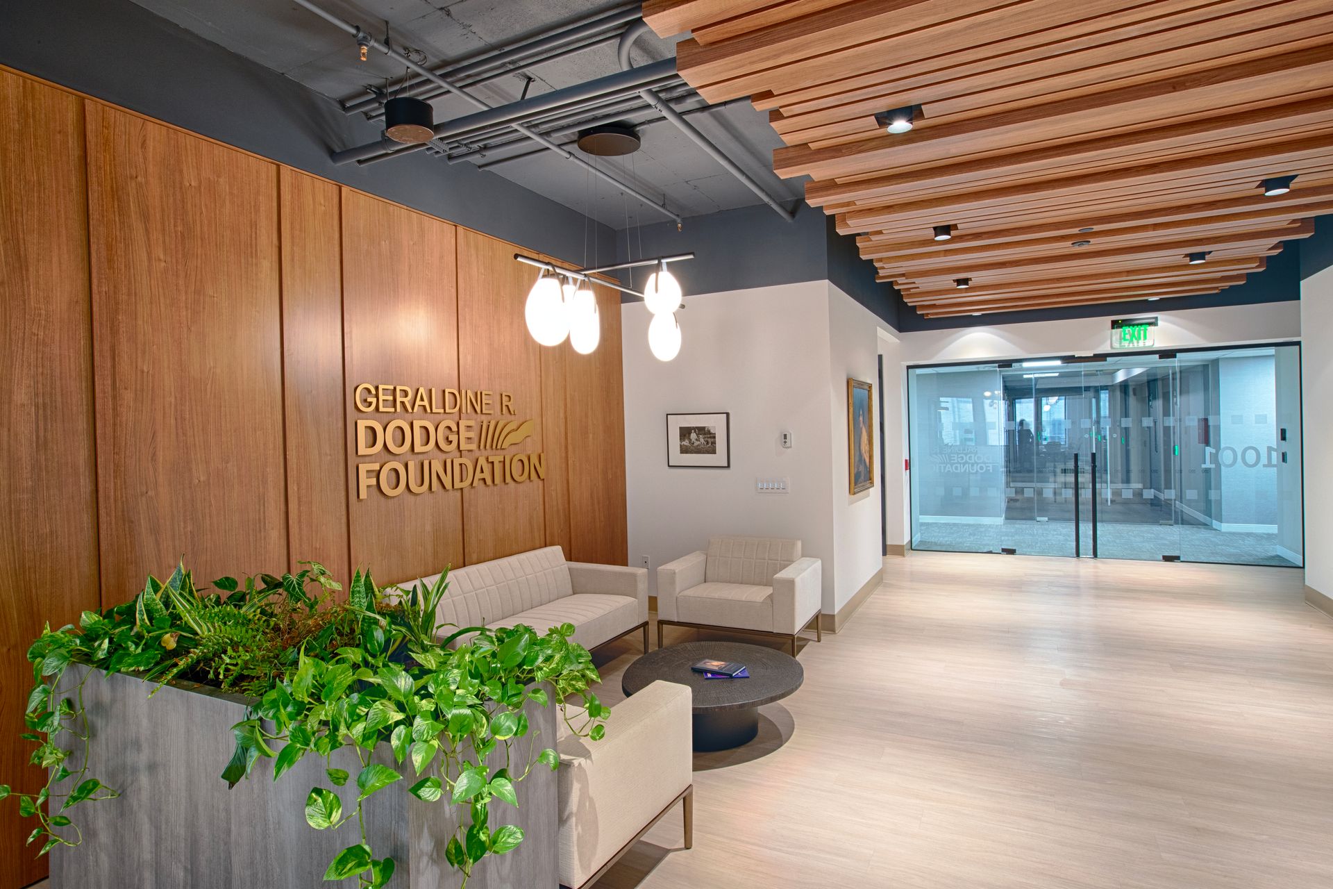 Reception area with seating, wooden wall with logo, and glass doors to offices.
