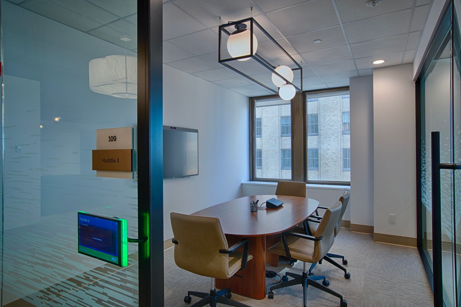 Conference room with oval table, chairs, TV, and view outside window. Neutral colors, modern style.