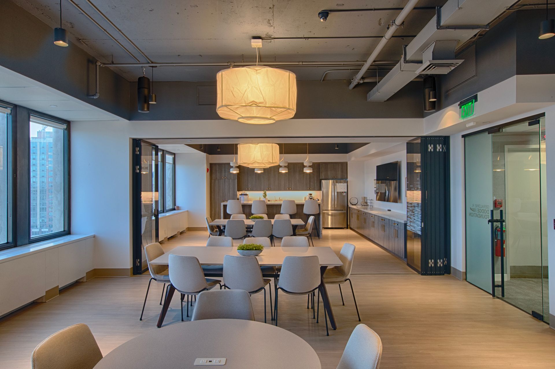 Modern office lounge with seating, kitchen, and windows overlooking a cityscape.