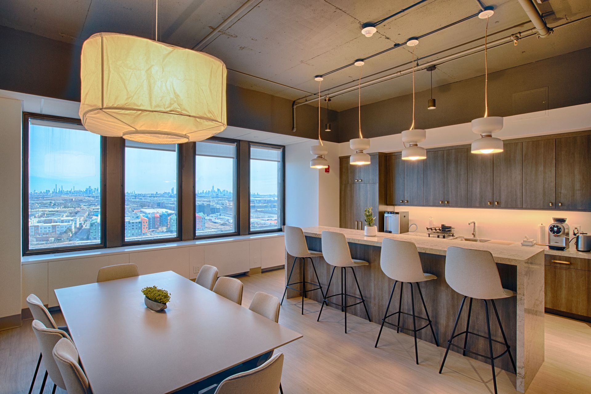 Modern office kitchen with long table and chairs, island with stools, and skyline views.