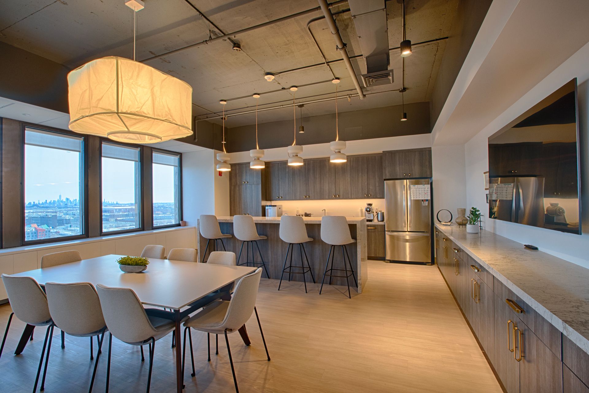 Modern office kitchen with a large table, bar, and city view.