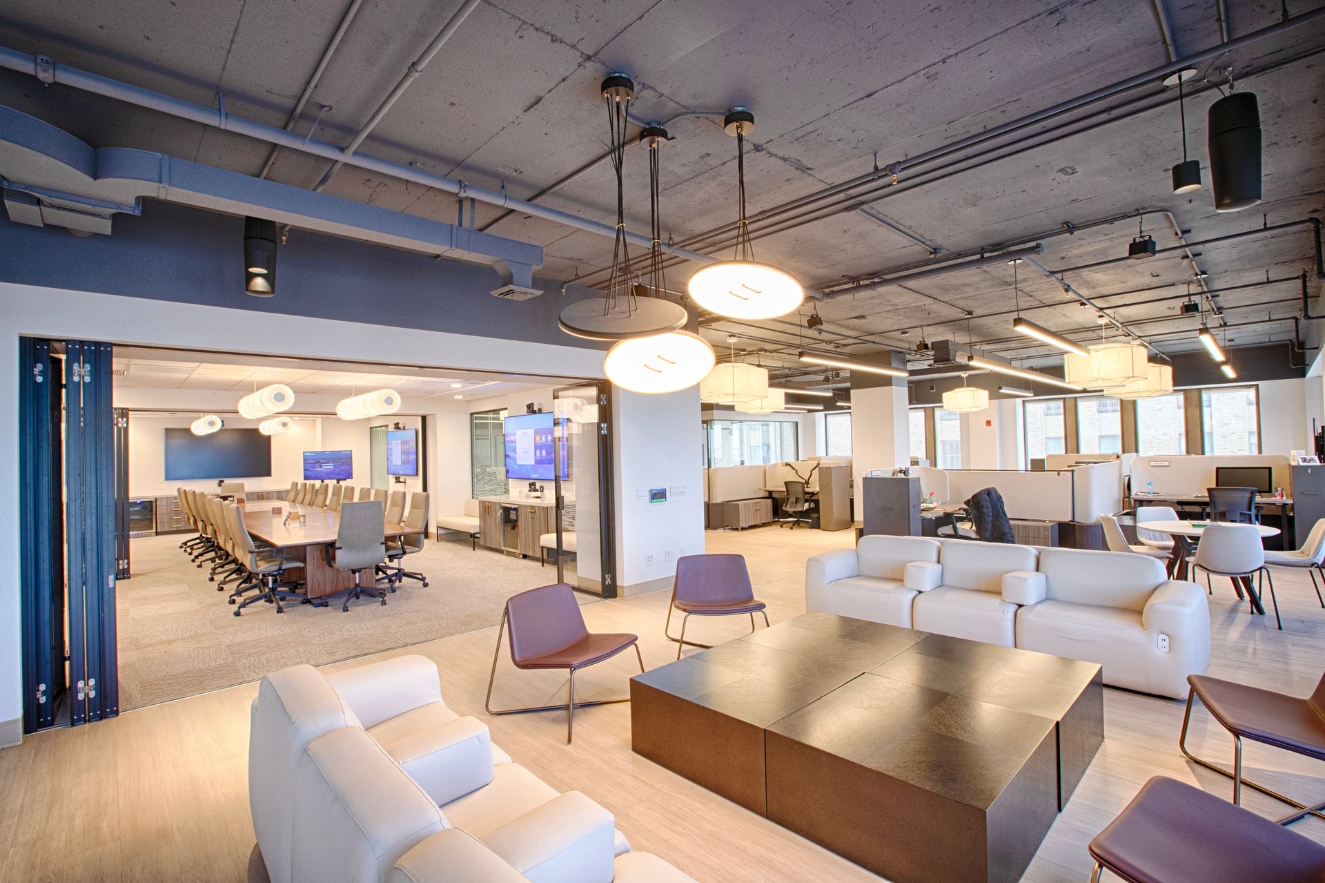 Modern office space with lounge area, conference room, and work cubicles. Neutral colors, natural light, and contemporary furniture.