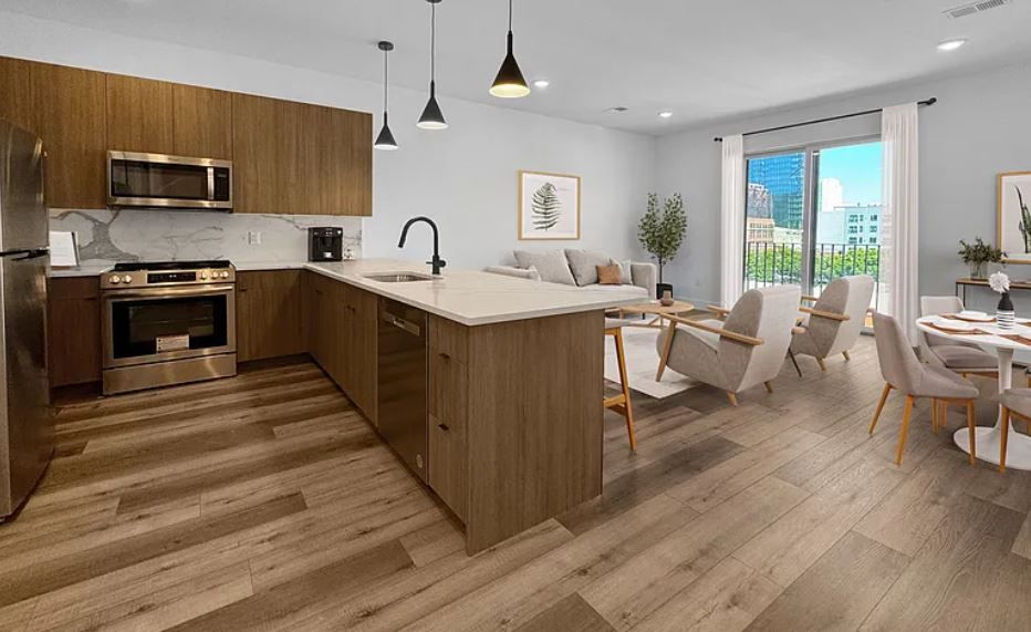 Modern open-concept living space with kitchen, dining area, and living room; light wood floors, blue walls, stainless steel appliances.