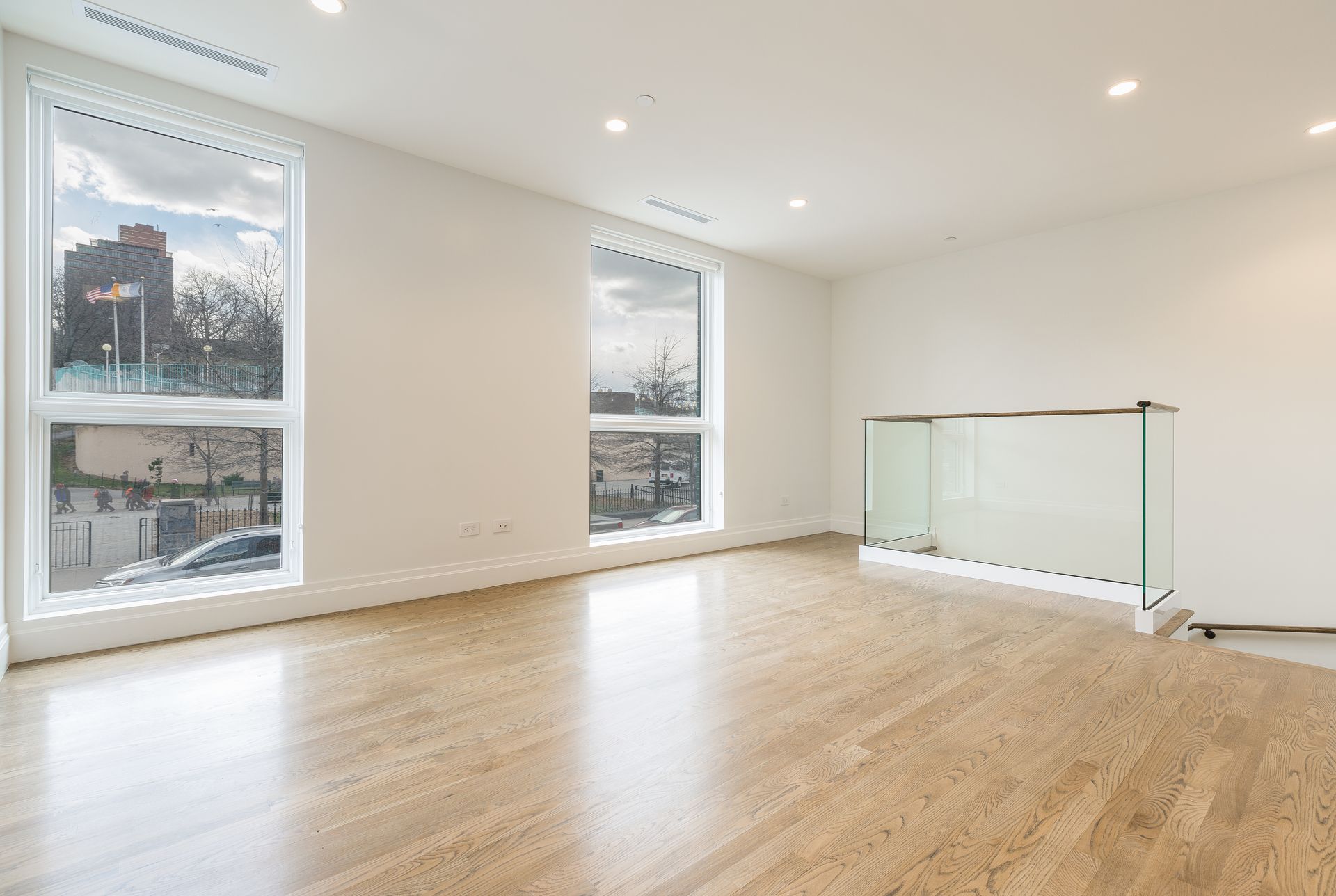 Empty, modern room with hardwood floors, large windows, and glass railing.