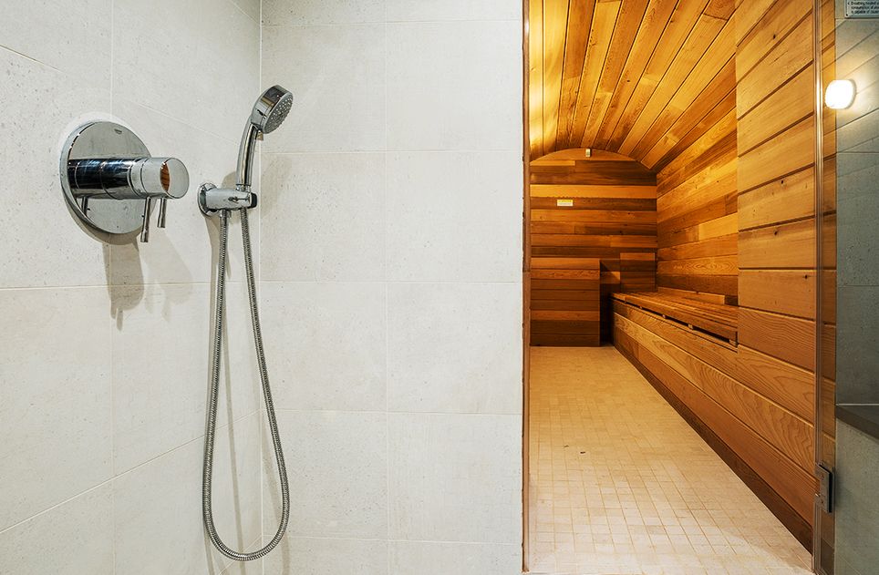 Shower stall with silver fixtures and a wooden sauna visible through the doorway.