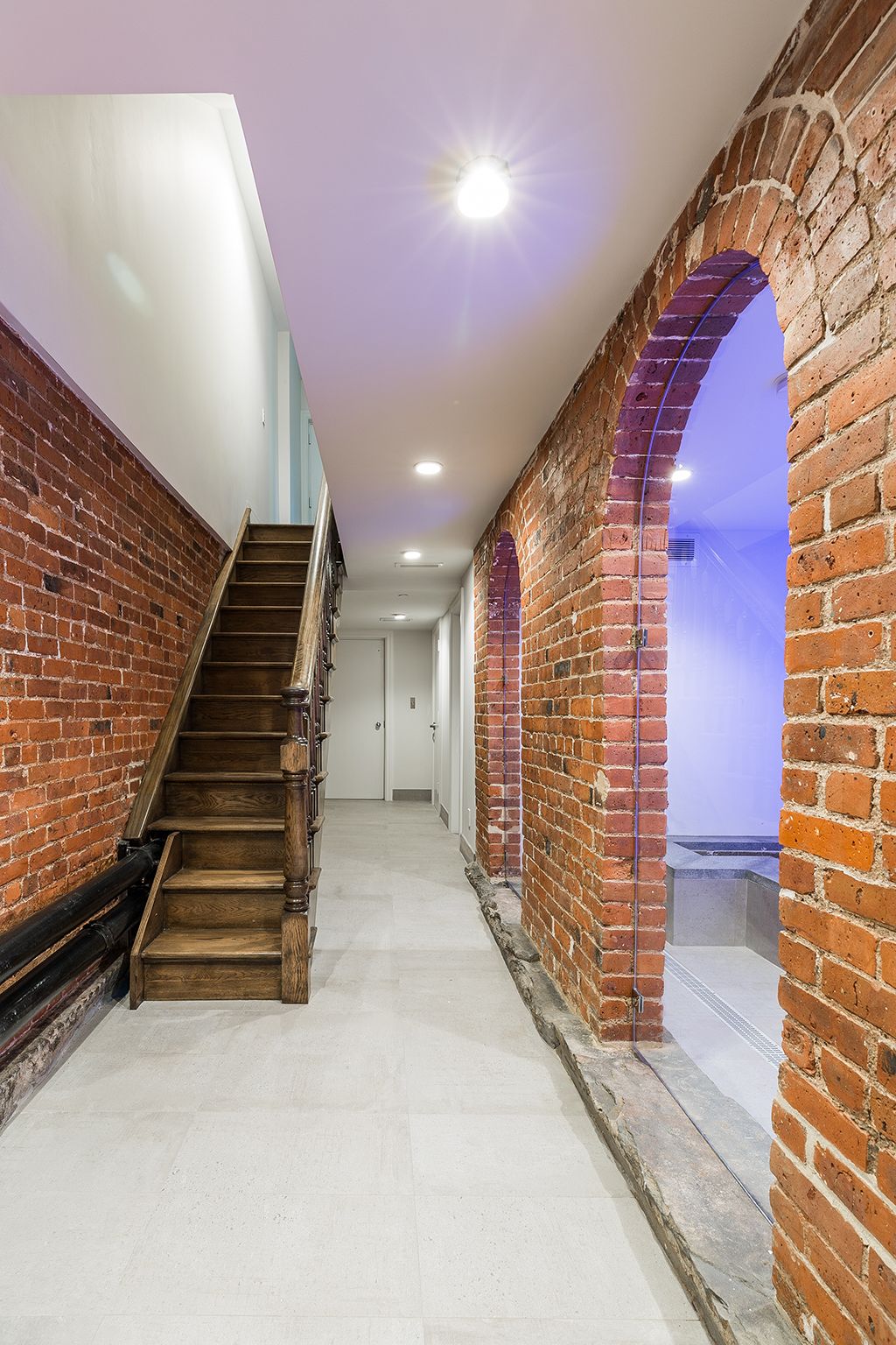 Long, narrow hallway with exposed brick walls, wooden stairs, and arched openings.