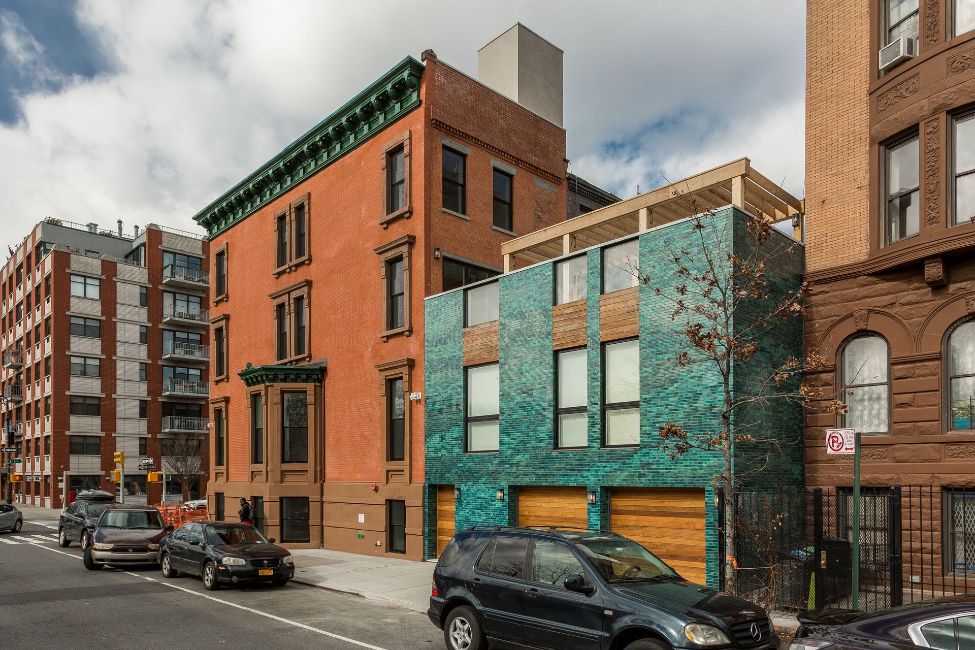 Street view of brick buildings, one teal with wood garage doors, cars parked on street.
