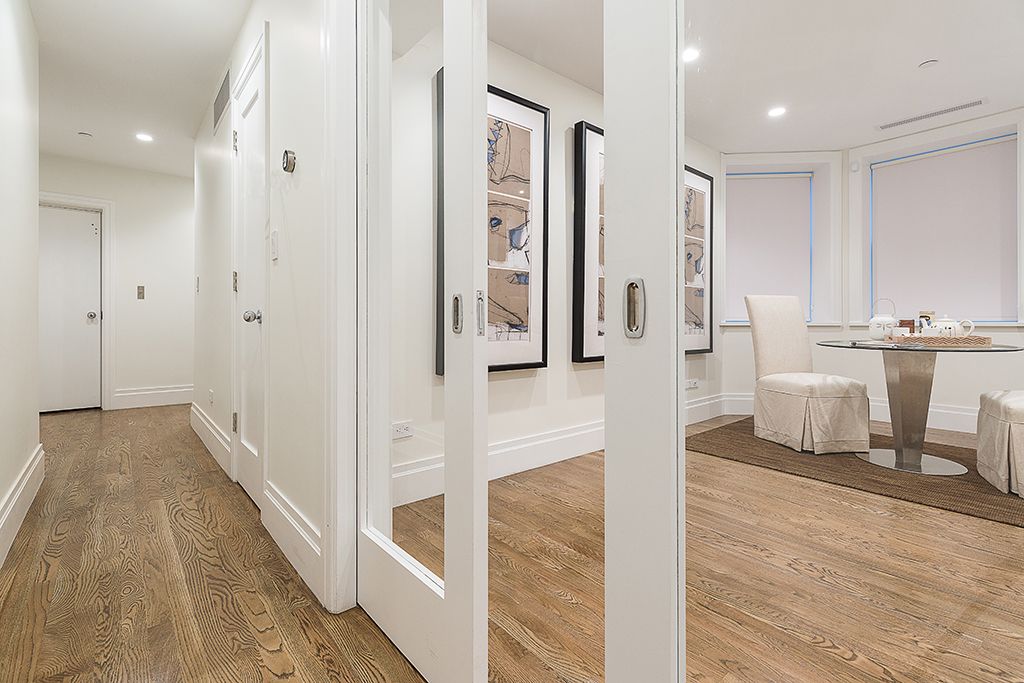 Hallway with white walls, wood floors, and pocket doors leading to a room with artwork, table, and chairs.