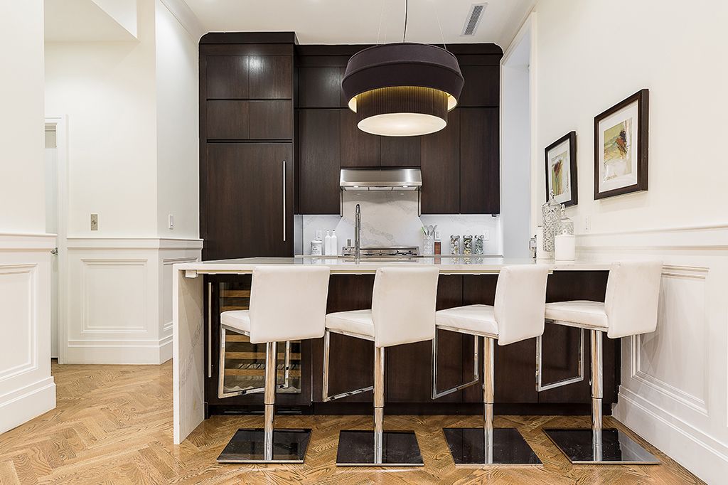 Modern kitchen with dark cabinetry, white island with bar stools, and pendant light.