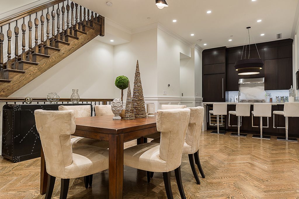 Dining area with a wooden table and chairs, kitchen with a bar, and a staircase.