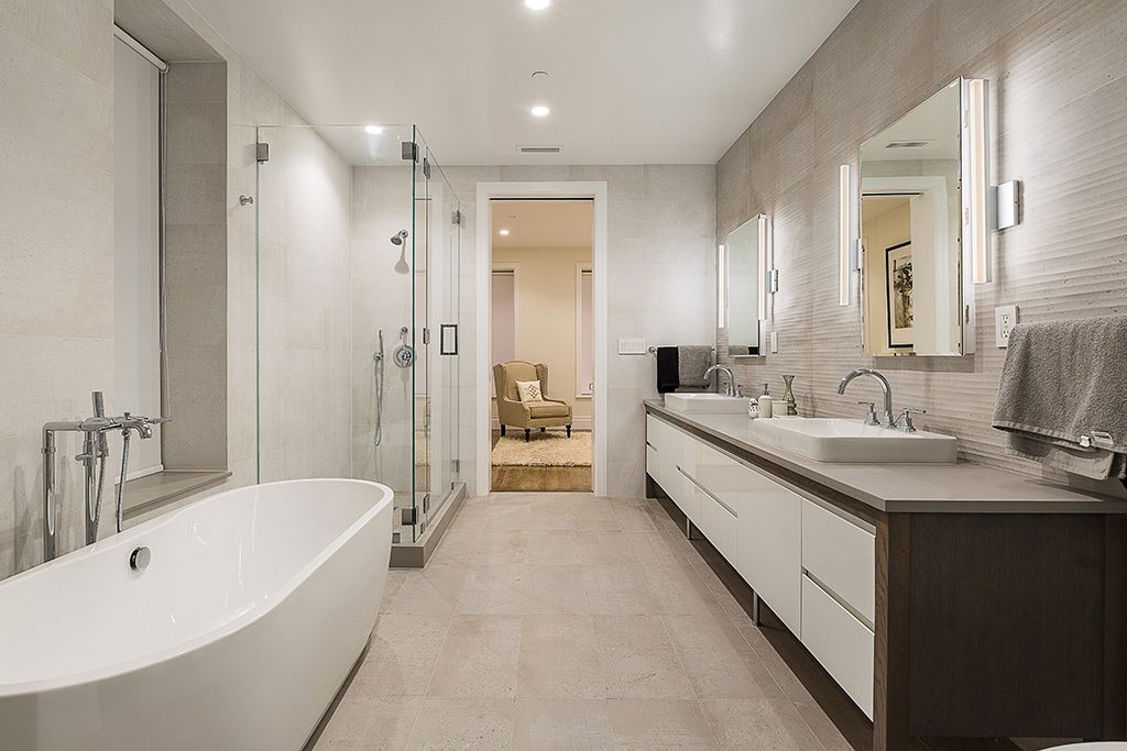 Modern bathroom with a bathtub, two sinks, and a walk-in shower. Neutral tones and bright lighting.