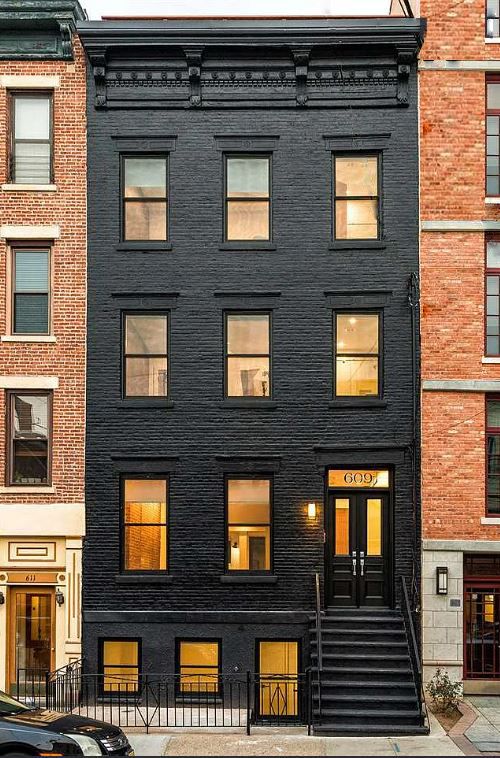 Black brick townhouse with three stories, black door, and staircase. Windows glow, a street scene.