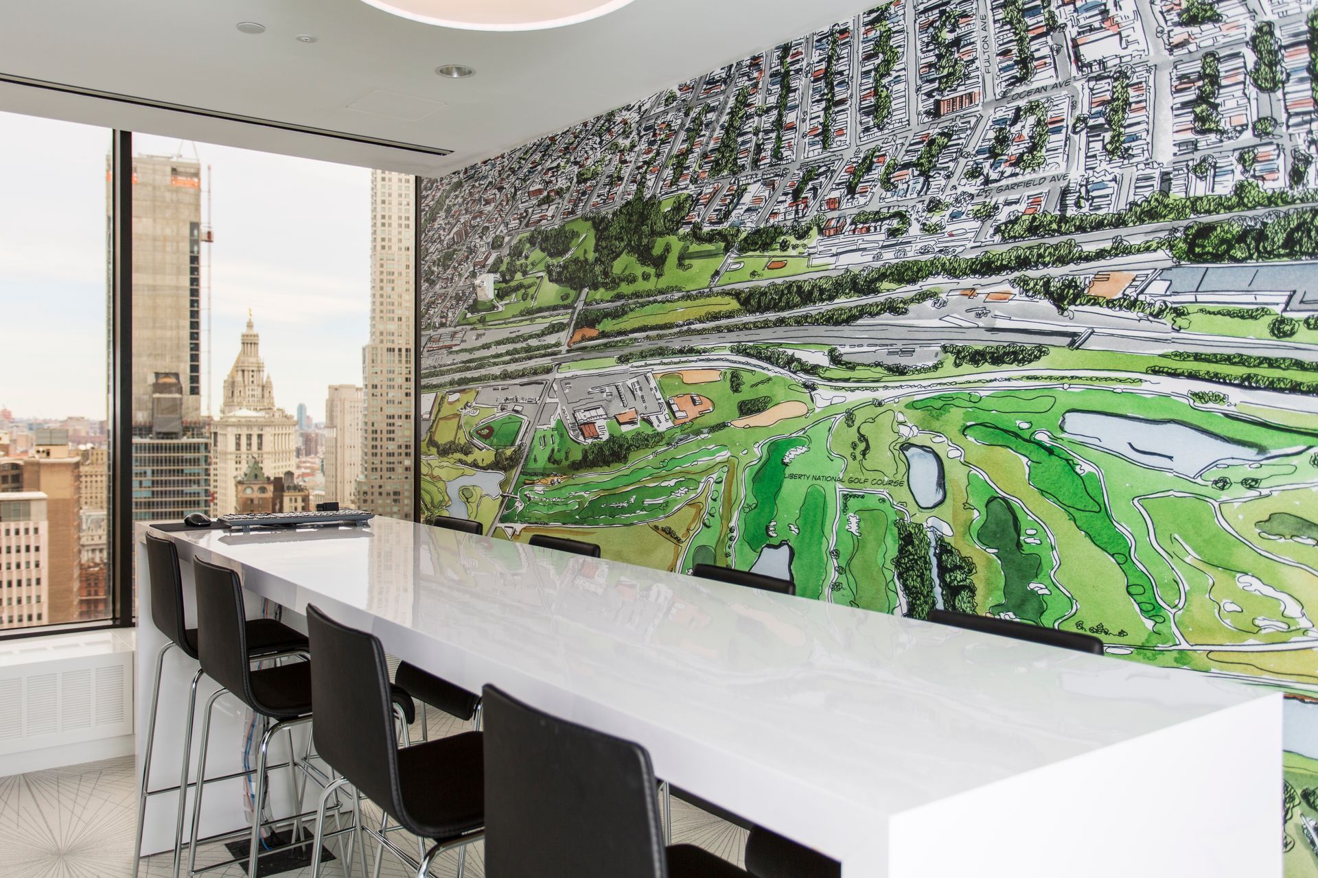 Modern office space with long white table, city view, mural of a golf course, and black chairs.