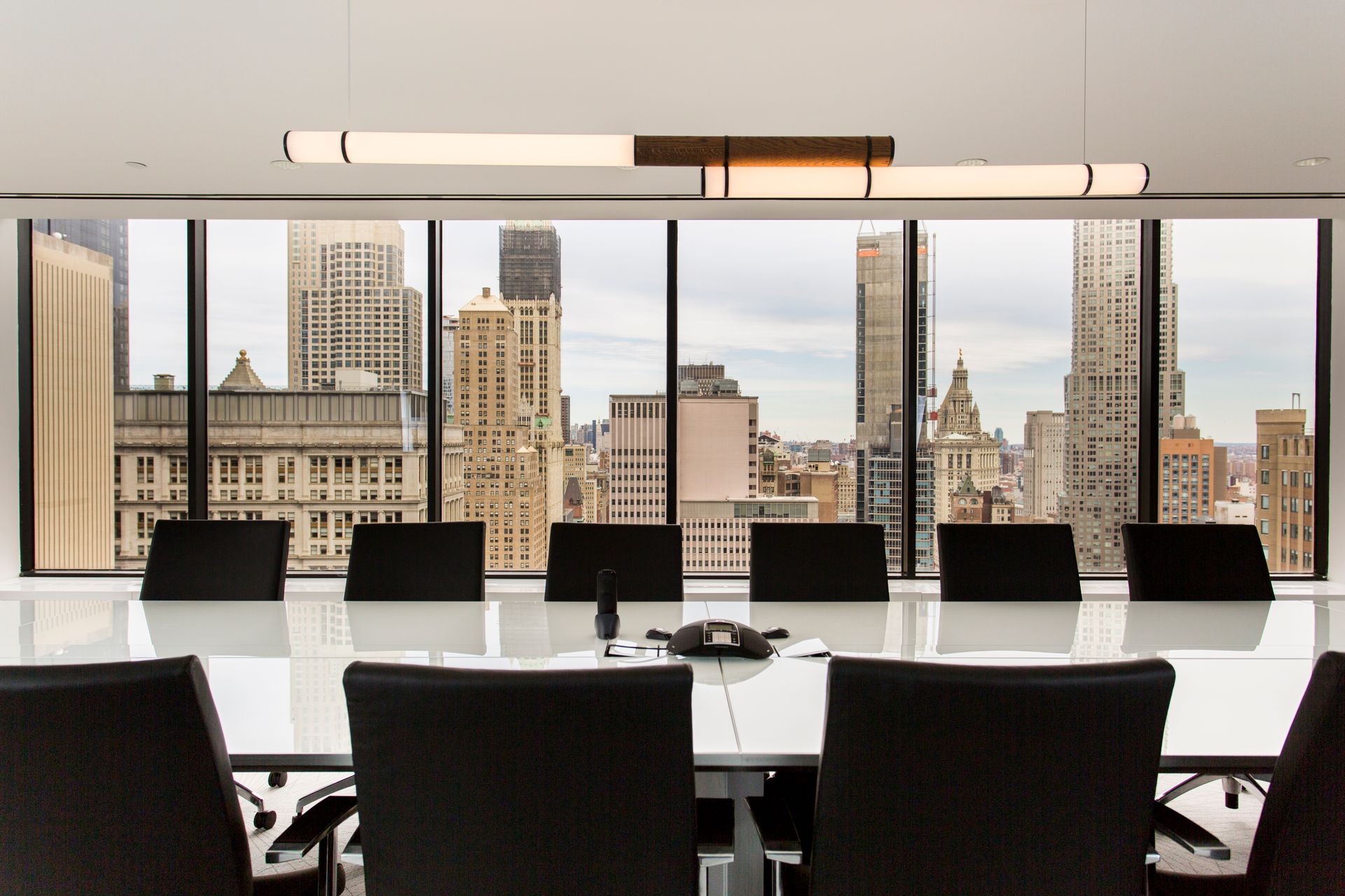 Conference room overlooking a cityscape with long table, black chairs, and modern lighting.
