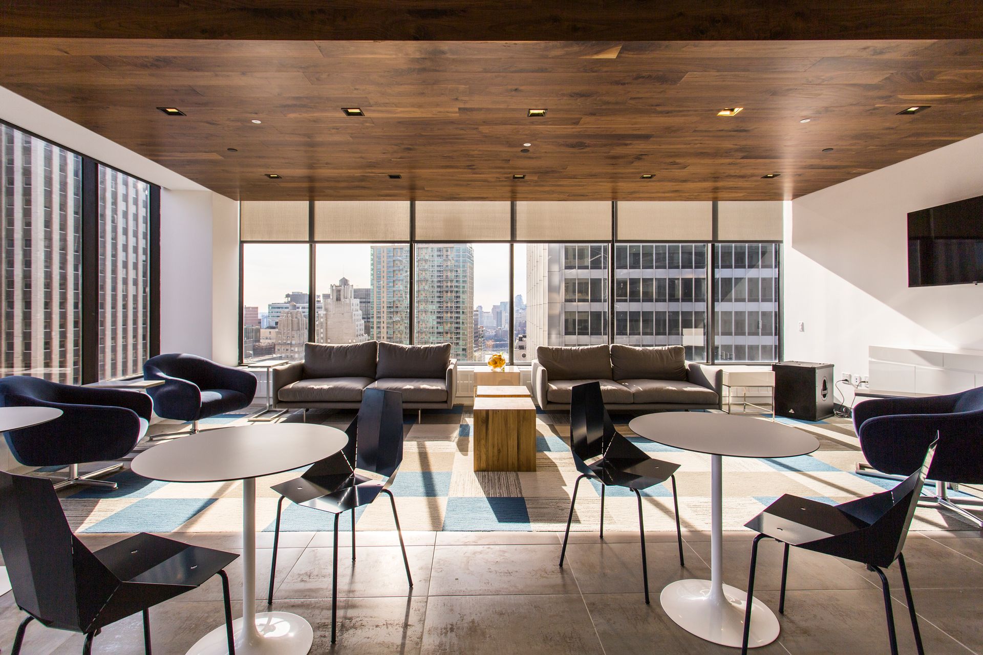 Lounge area with city view, featuring couches, chairs, tables, and a wooden ceiling.