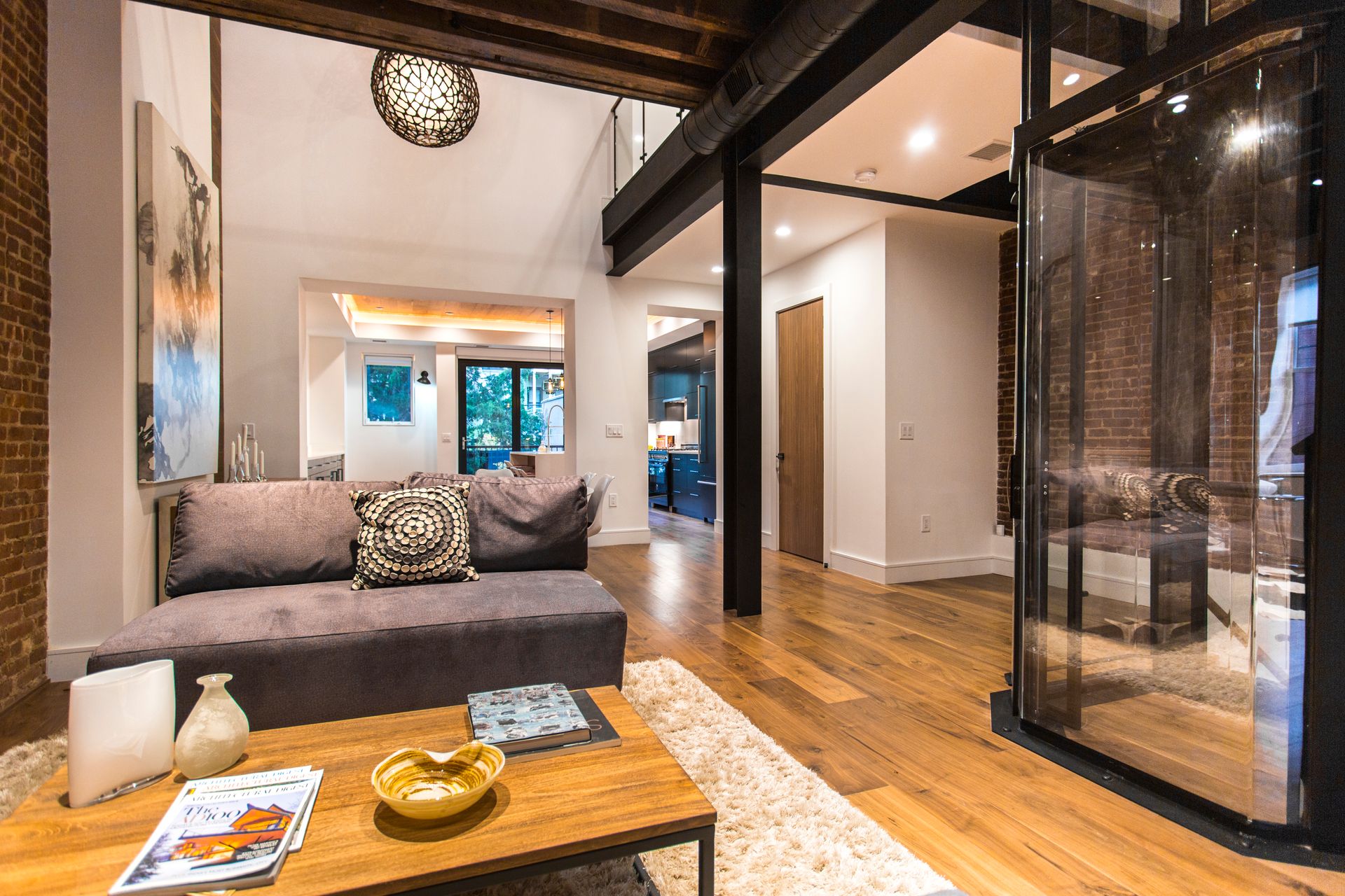 Living room with exposed brick, wooden floor, gray sofa, and modern glass enclosure.