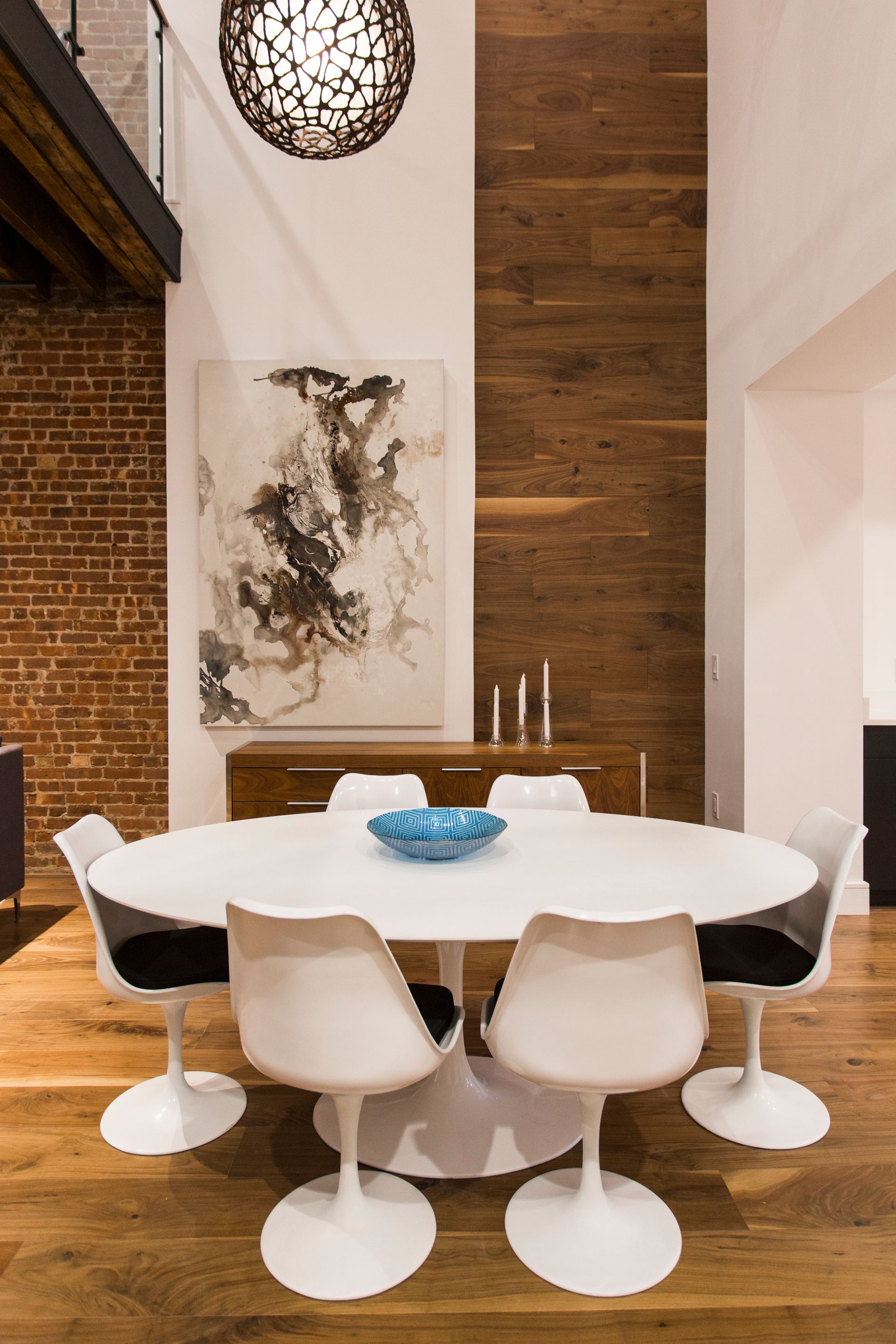 Modern dining room with oval white table, white chairs, artwork, and wood accent wall.