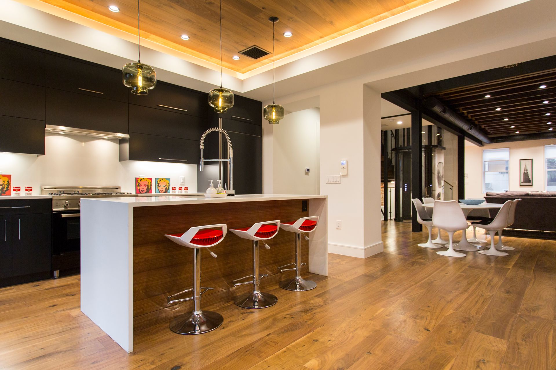 Modern kitchen with island, red bar stools, and pendant lights. Wood floor and ceiling.