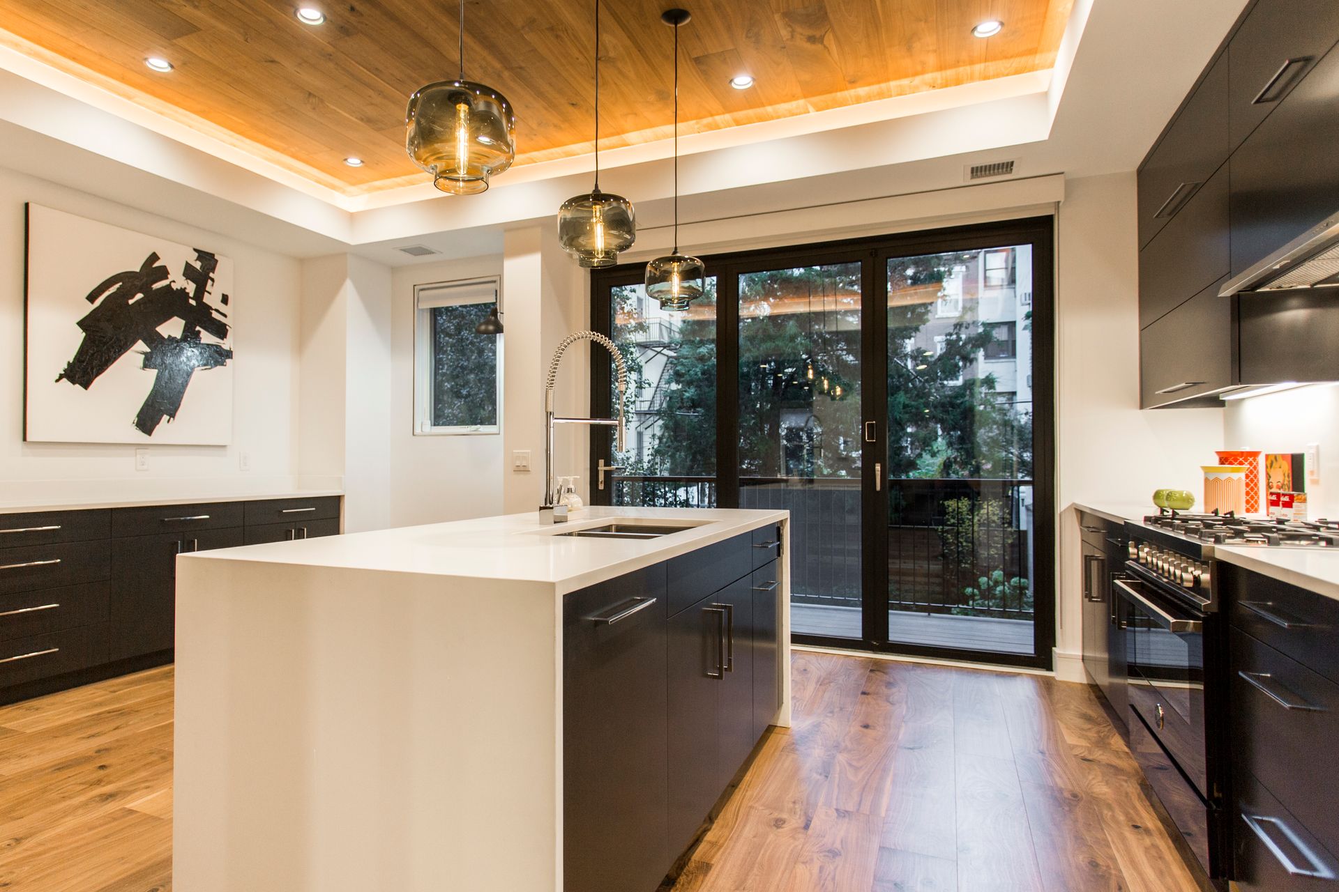 Modern kitchen with wood ceiling, dark cabinets, island with sink, and sliding glass doors.