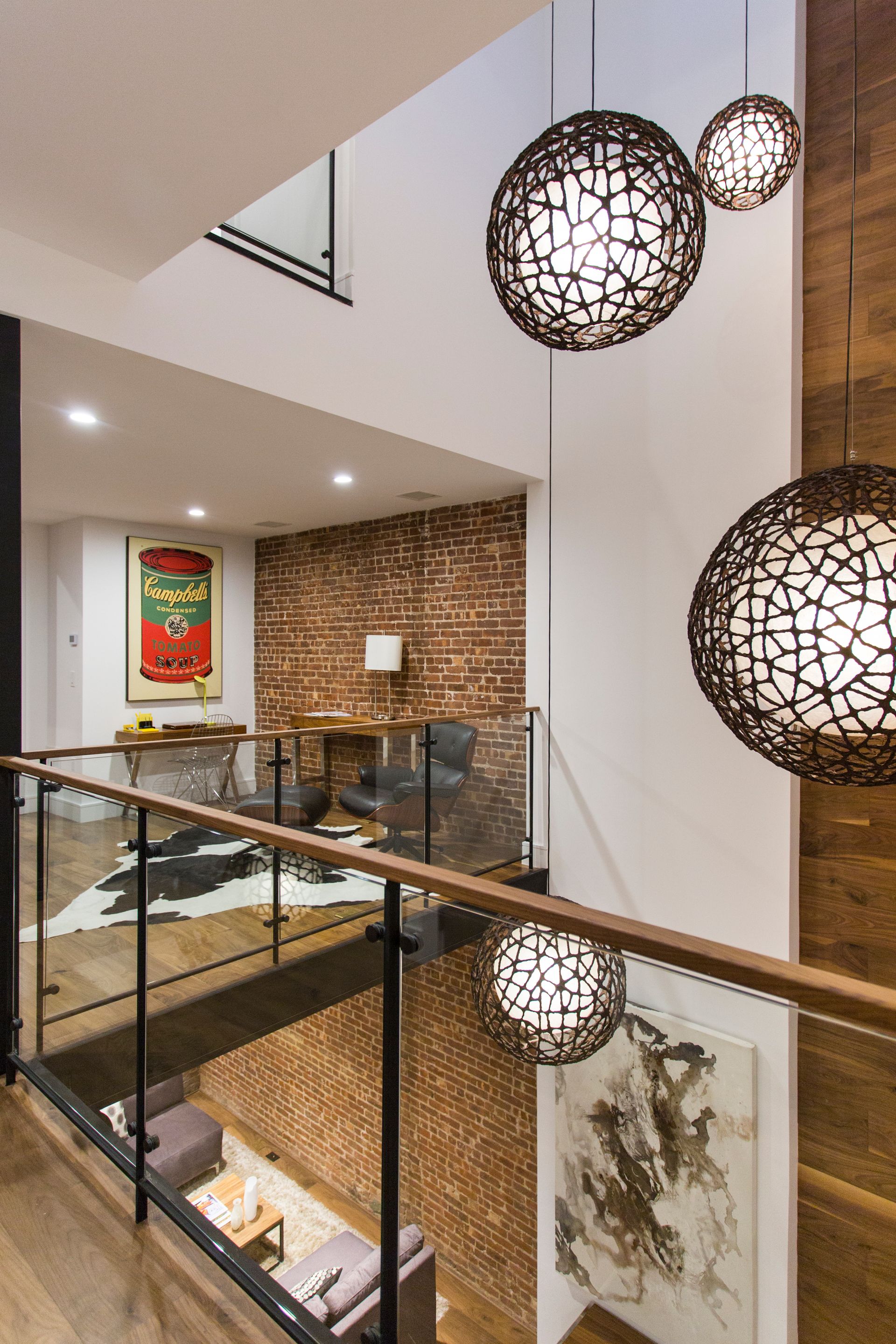 Modern loft interior with globe pendant lights, exposed brick, glass railings, and a cowhide rug.