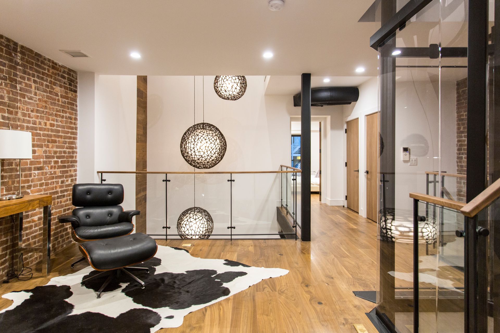 Modern interior with exposed brick, leather chair, cowhide rug, pendant lights, and glass railing.