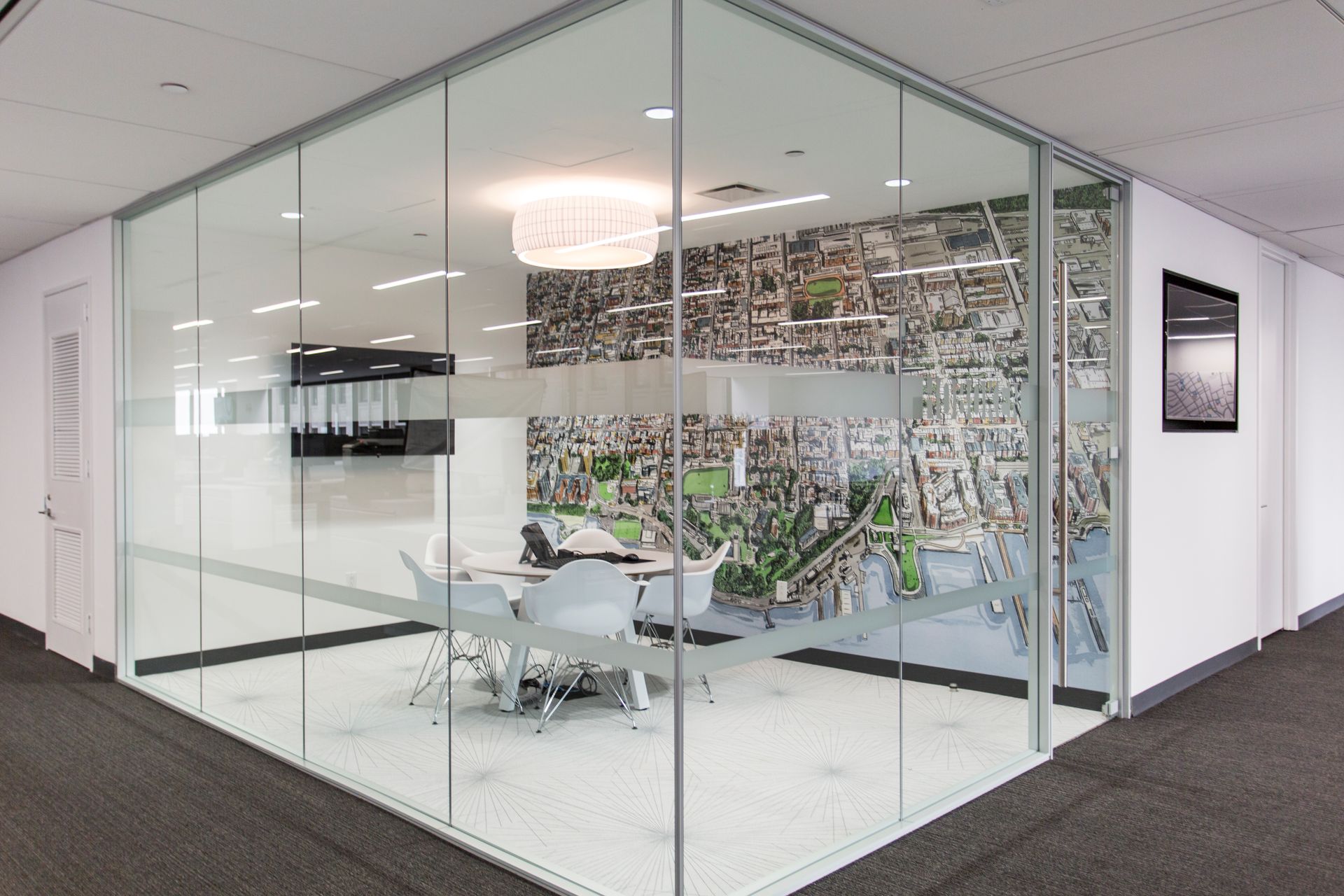 Glass-walled conference room in an office. White walls, carpet, meeting table, and a city image on the back wall.