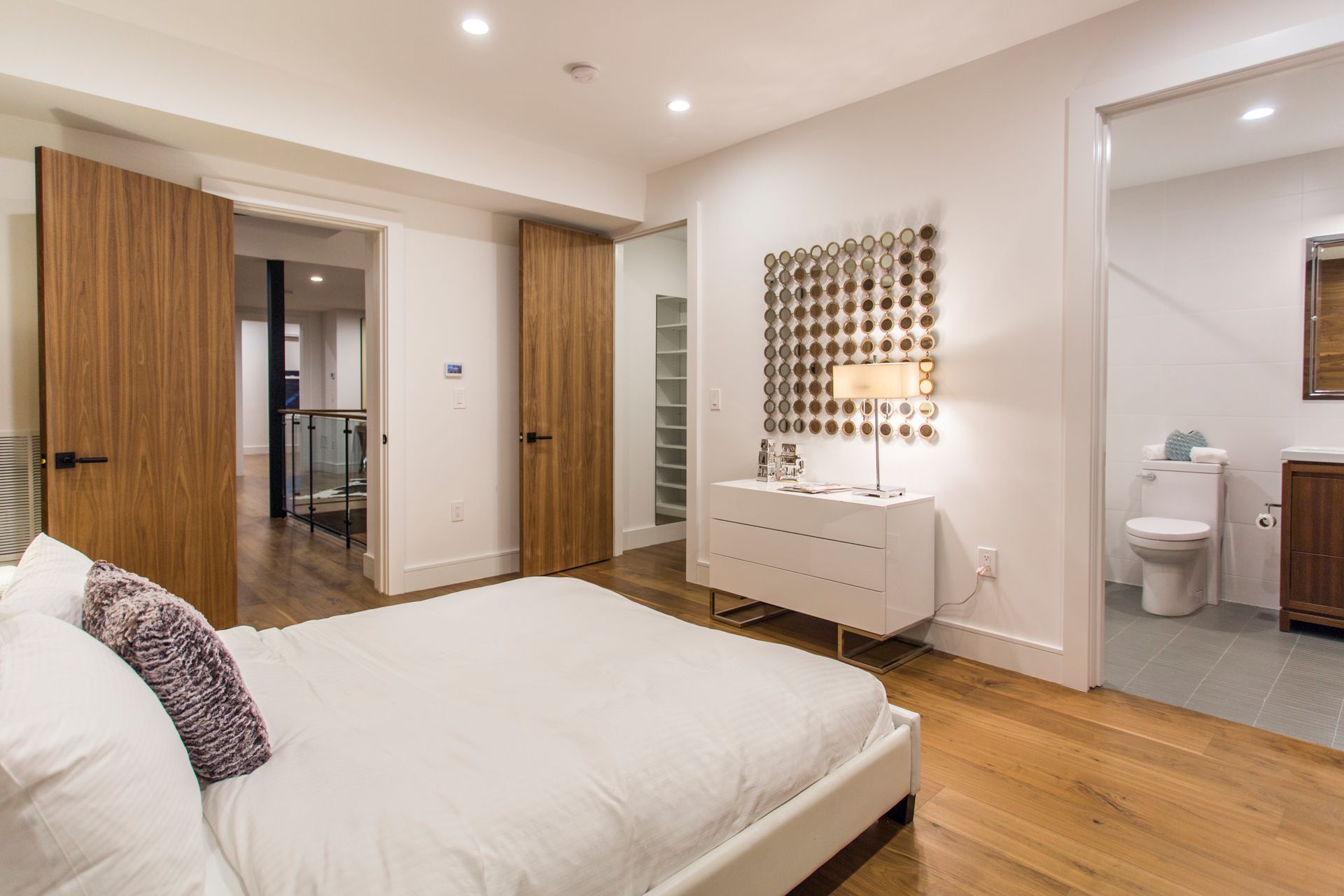 Bedroom with wooden floors, white walls, and a bed. Two doors lead to other rooms, one to a bathroom.