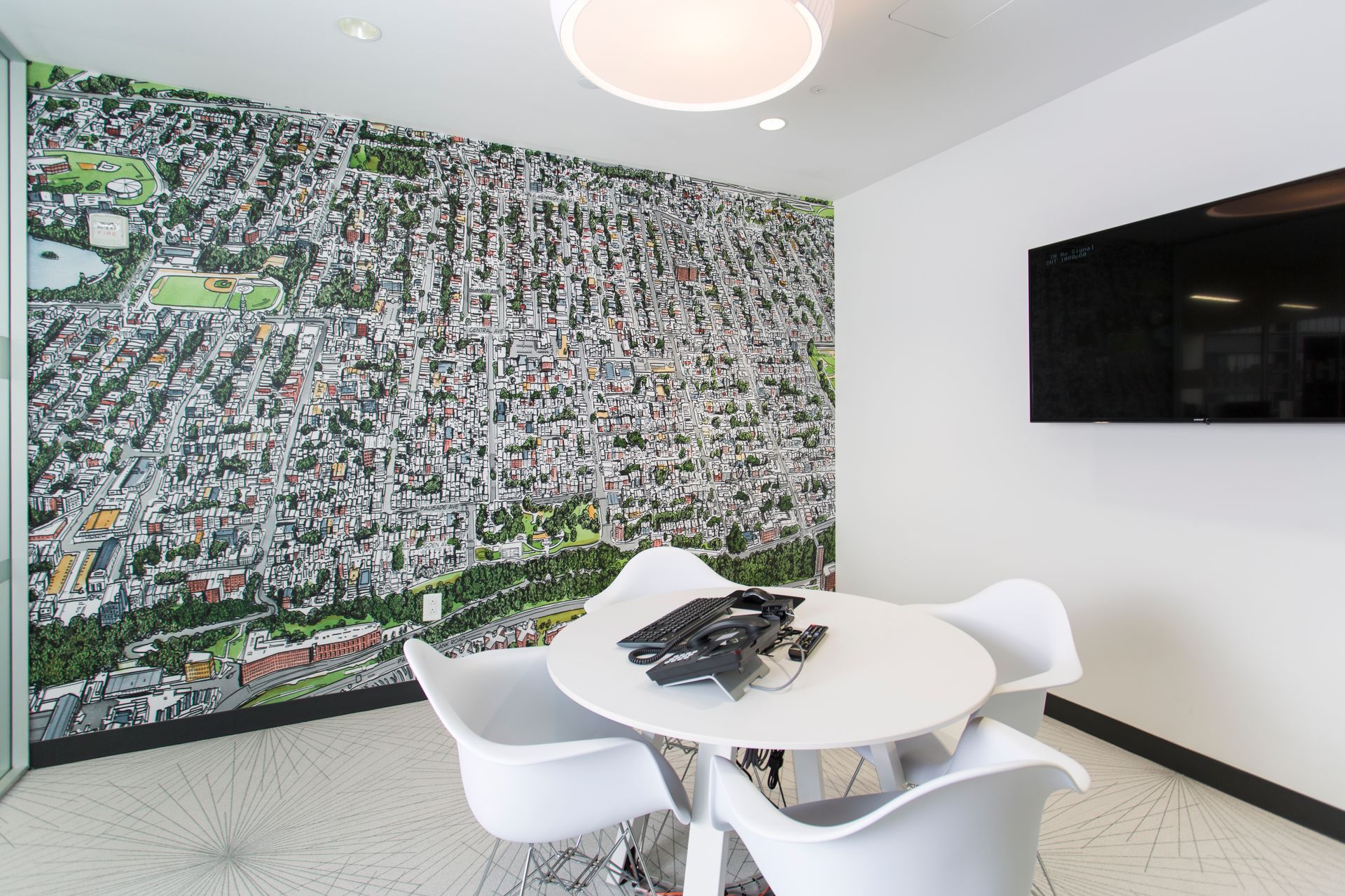 Meeting room with city map mural, white table, chairs, and TV screen.