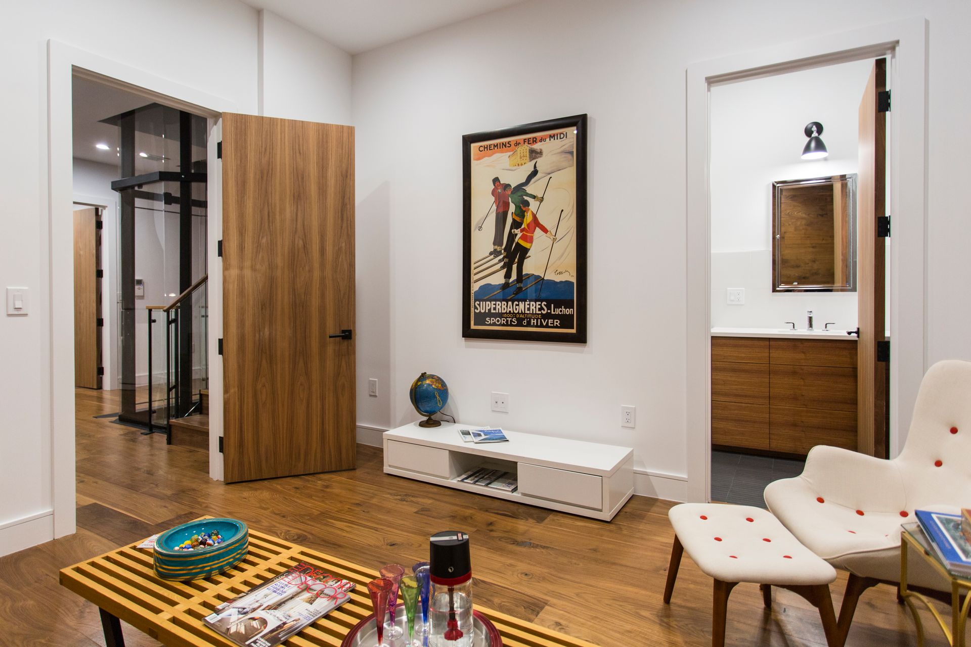 Living room with hardwood floors, wooden doors, and ski poster. Contains a sofa and an ottoman.