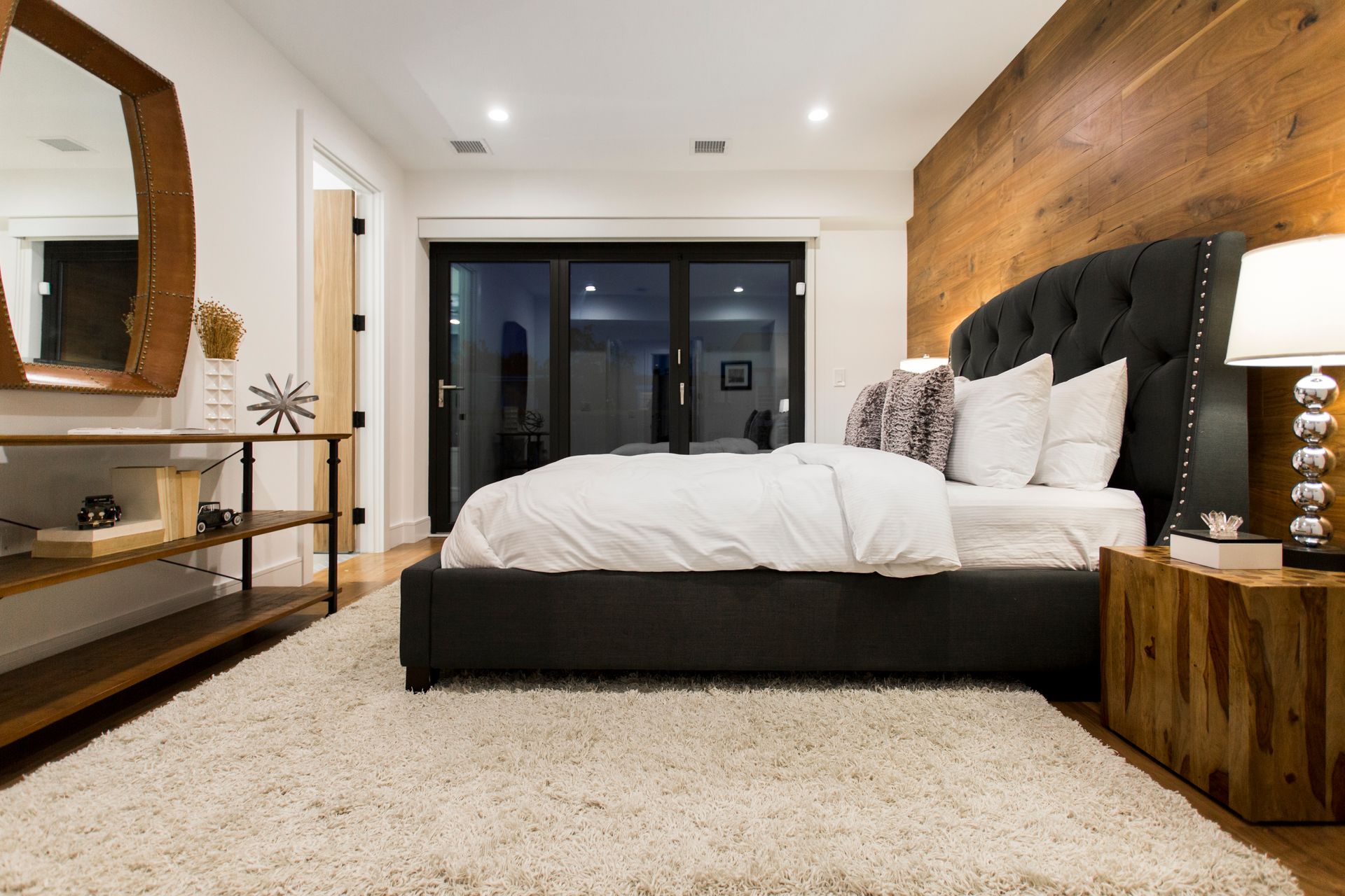 Bedroom with a gray upholstered bed, wooden accent wall, and a large rug.