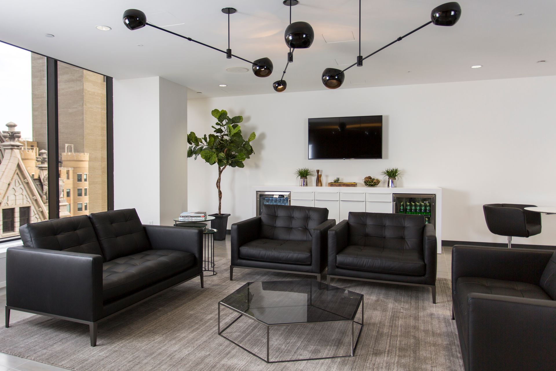 Modern office waiting area with black furniture, a gray rug, and abstract black light fixture.