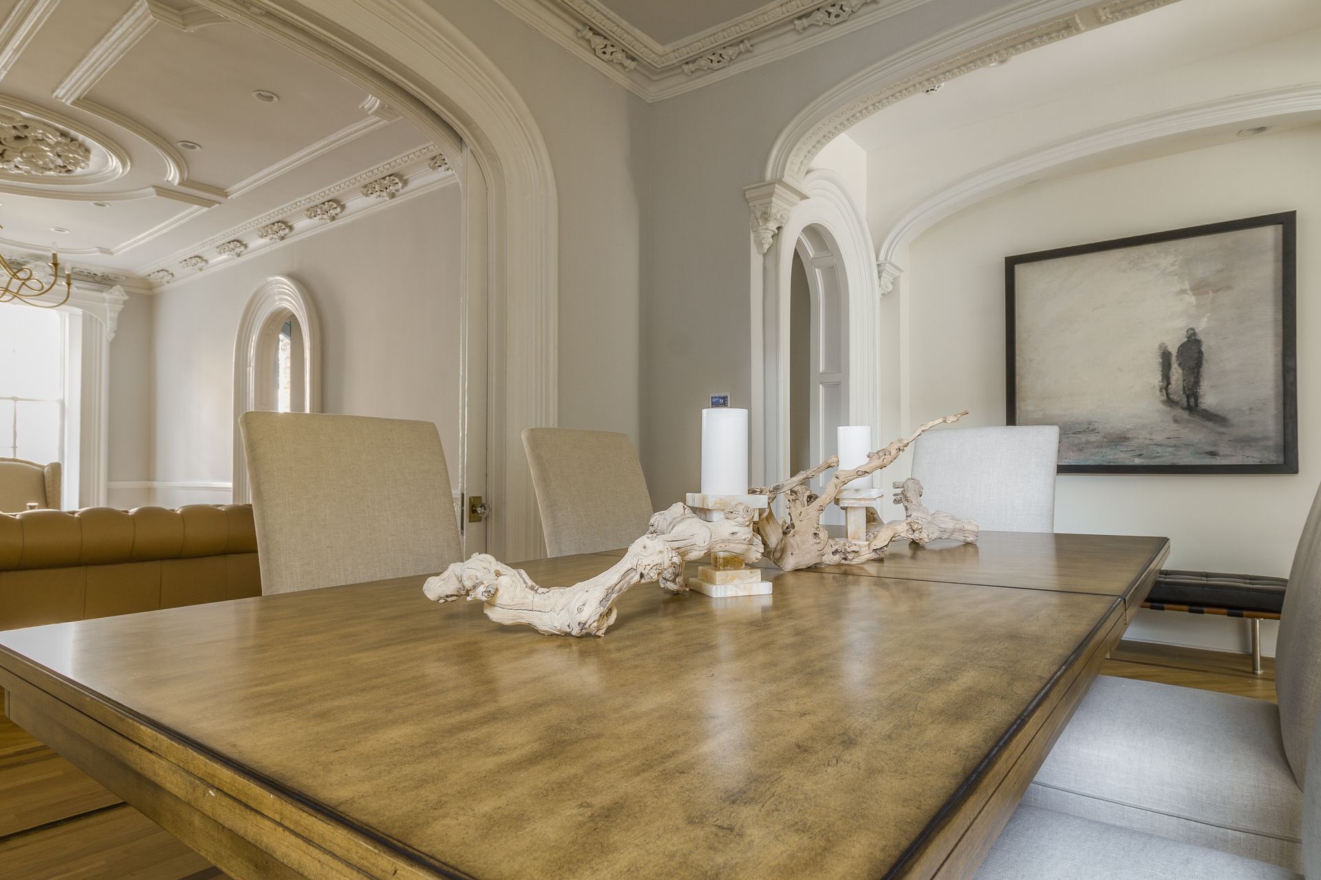 Dining room with large wood table, white chairs, coral decor, and a framed painting.