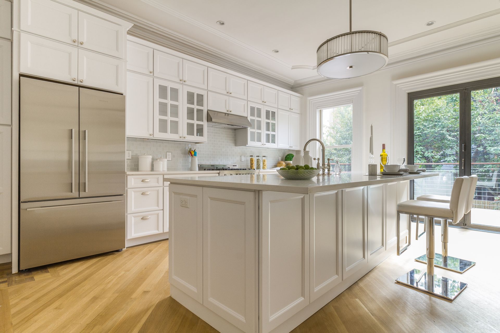 White kitchen with island, stainless steel refrigerator, light wood floors, and outdoor access.