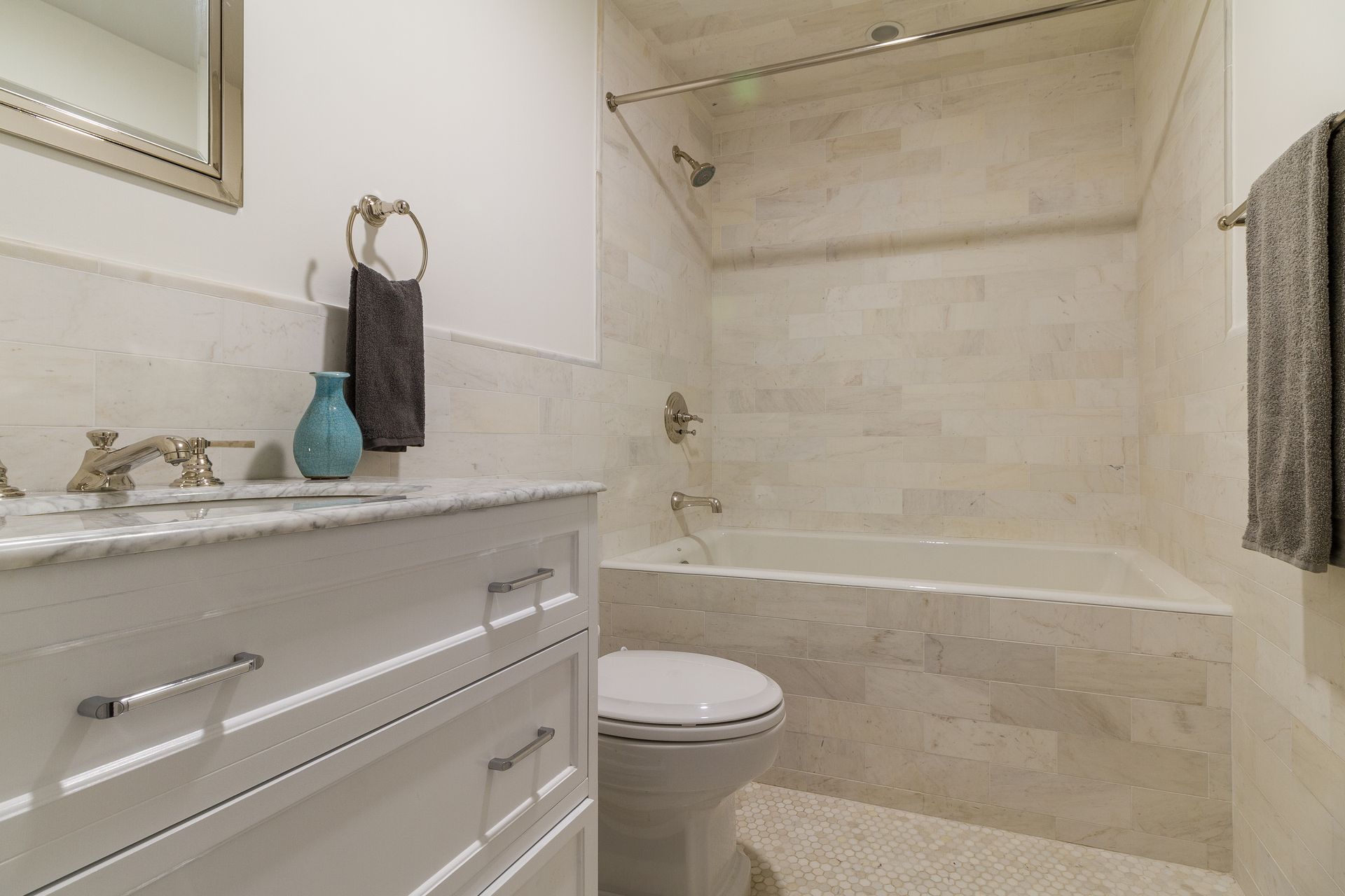 White bathroom with marble vanity, bathtub, toilet, and towel rack.