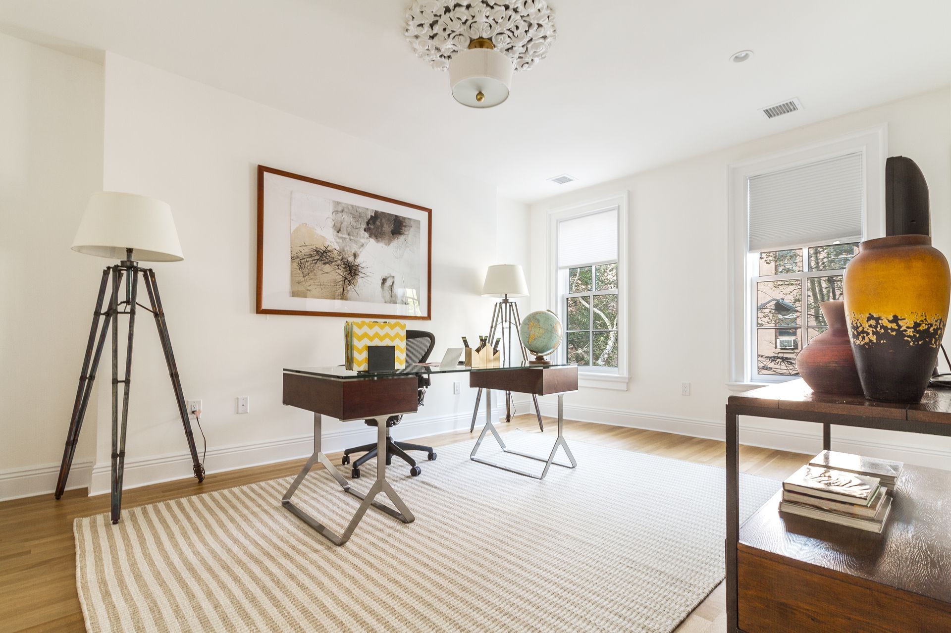 Bright home office with two desks, art, rugs, and windows.